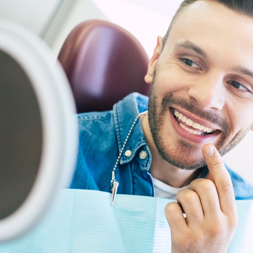 Check out. A mirror in a hand of a nice-looking man with a perfect smile which he is using for checking the final look of his smile.
